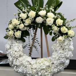 White rose and hydrangea wreath on an easel with dark green leaves