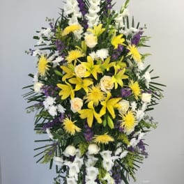 Tall funeral spray with yellow lilies, white roses, and purple accents