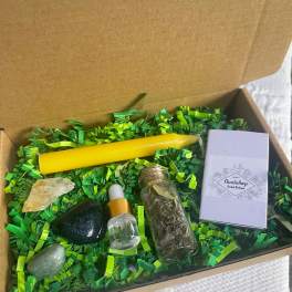Gift box with a yellow candle, crystals, a dropper bottle, and a small herb vial