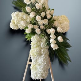 White floral cross on an easel with roses and hydrangeas