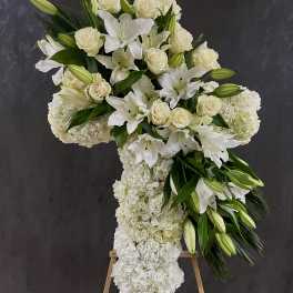 White floral cross arrangement on an easel with lilies and roses