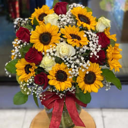 Bouquet of sunflowers and red and white roses in a glass vase with a red ribbon