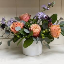 Peach roses and lavender flowers in a white vase