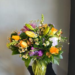 Mixed bouquet of lilies, roses, and purple flowers in a glass vase