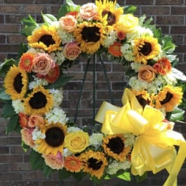 Standing wreath of sunflowers, roses, and other bright blooms with a large yellow bow on an easel