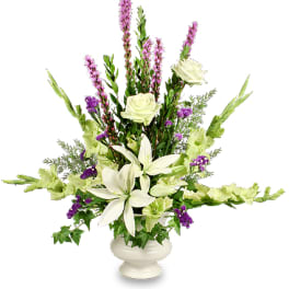 Tall white and purple floral arrangement with lilies and roses in a white pedestal vase