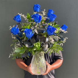 Blue roses arranged in a clear glass vase with mixed greenery