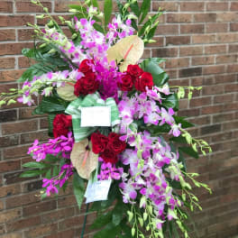 Standing spray of purple orchids, red roses, and pale anthuriums on a display easel