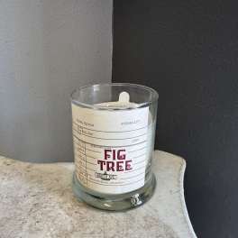A glass candle jar with a Fig Tree label sits on a small table.