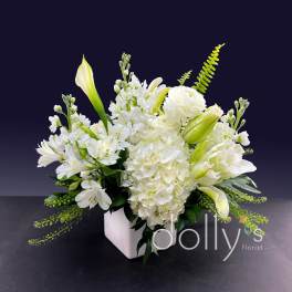 White floral arrangement in a square vase with lilies and hydrangeas
