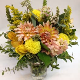 Mixed yellow and peach flowers arranged in a clear glass vase