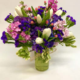 Colorful bouquet of tulips, purple blooms, and pink flowers in a green glass vase