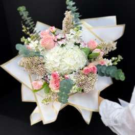 Bouquet of pink and white flowers wrapped in white paper with gold trim