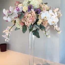 Tall pastel floral arrangement in a clear glass vase with orchids and hydrangeas