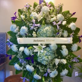 Large sympathy spray with white and lavender flowers and a "Beloved Sister" ribbon