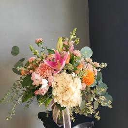 Mixed bouquet with pink lilies, cream hydrangea, and orange blooms in a glass vase