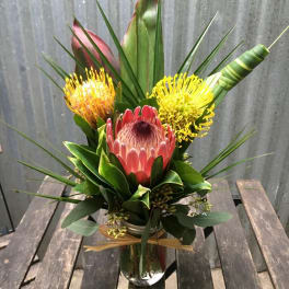 Tropical-style bouquet with pink and yellow protea in a clear glass jar vase