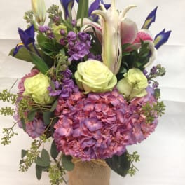 Bouquet of pink hydrangeas, lilies, irises, and pale roses in a burlap-wrapped vase