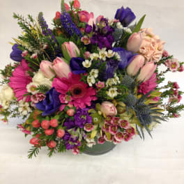 Mixed bouquet of pink, purple, and white flowers in a round vase