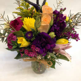 Mixed bouquet of purple, yellow, and peach flowers in a glass vase