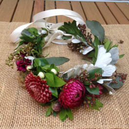 Floral wreath with pink blooms and white ribbon on a burlap mat