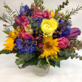 Colorful mixed bouquet in a clear glass vase with sunflowers and tulips