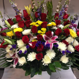 Large mixed bouquet of red roses, lilies, and white chrysanthemums in a white container