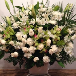 Large white floral arrangement with lilies, roses, and orchids in a pale vase