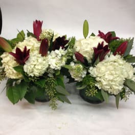 Two white floral arrangements with burgundy lilies in dark containers