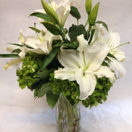 White lilies arranged in a clear glass vase with green blooms