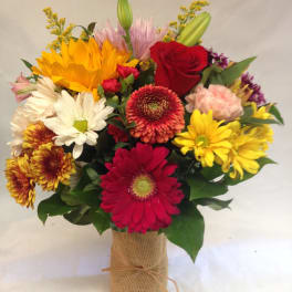 Mixed bouquet with sunflowers, roses, and daisies in a burlap-wrapped vase