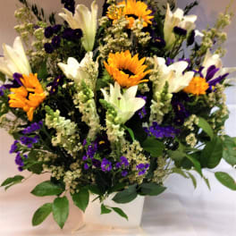 Bouquet of white lilies, sunflowers, and purple flowers in a white vase