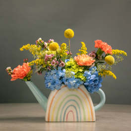 Colorful flowers arranged in a pastel watering can vase with a rainbow design