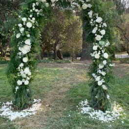 White floral arch covered in roses and greenery outdoors