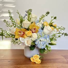 Bouquet of white roses, blue hydrangeas, and yellow orchids in a white vase