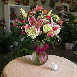 Pink lilies and hydrangeas arranged in a glass vase with a ribbon