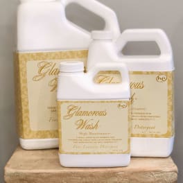 Three white laundry detergent jugs with gold labels stacked on a decorative pedestal.