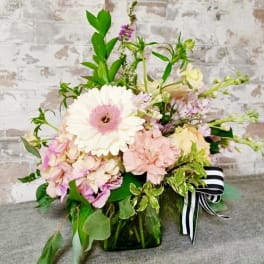 Pastel flower arrangement in a green glass vase with a striped ribbon