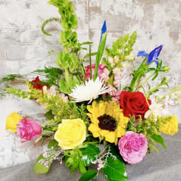 Colorful mixed flower arrangement in a metal container with roses and sunflowers