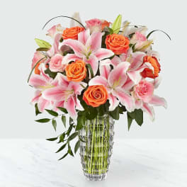 Pink lilies and orange roses arranged in a clear glass vase