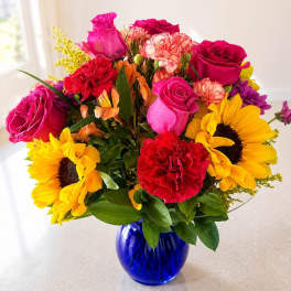 Mixed bouquet of roses, sunflowers, and carnations in a blue glass vase