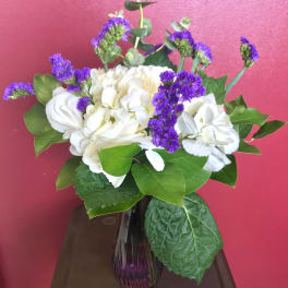 White hydrangeas and purple filler flowers in a glass vase