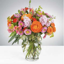 Mixed bouquet of orange and pink flowers in a clear glass vase