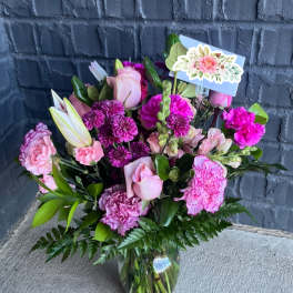 Pink and purple bouquet in a glass vase with a floral card