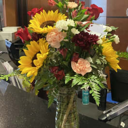 Mixed bouquet with sunflowers, roses, carnations, and alstroemeria in a glass vase