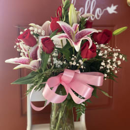 Bouquet of red roses and pink lilies in a glass vase with a pink ribbon