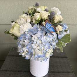 White roses and blue hydrangeas in a white vase with a butterfly accent
