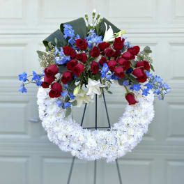 Red roses, blue flowers, and white lilies in a white chrysanthemum wreath