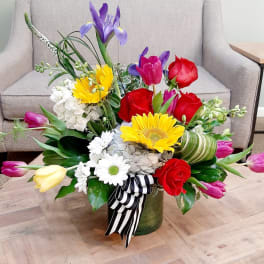 Colorful mixed flower arrangement in a green vase with a striped ribbon