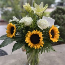 Bouquet of sunflowers, white roses, and pale lilies in a glass vase